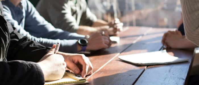 people sitting on chair in front of table while holding pens during daytime